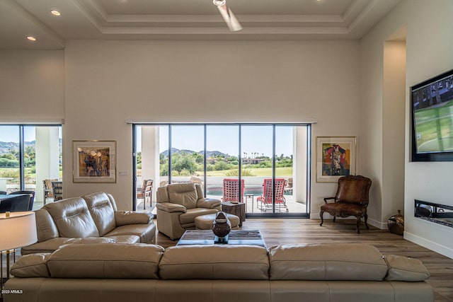 living area featuring a tray ceiling, a healthy amount of sunlight, a towering ceiling, and wood finished floors