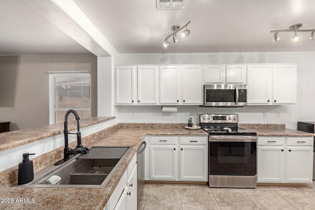 kitchen with appliances with stainless steel finishes, a sink, rail lighting, white cabinetry, and visible vents