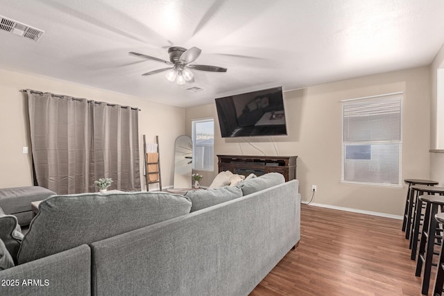 living area featuring a ceiling fan, baseboards, visible vents, and wood finished floors