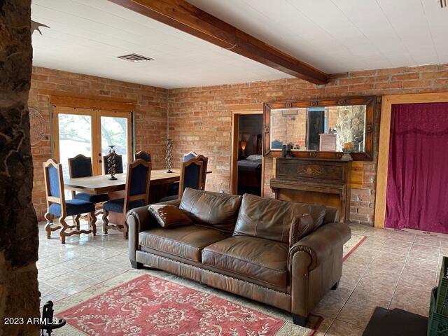 living room featuring light tile flooring, brick wall, and beamed ceiling