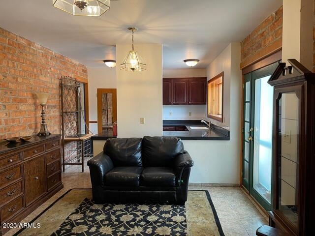 living room with sink, a notable chandelier, brick wall, and light tile floors