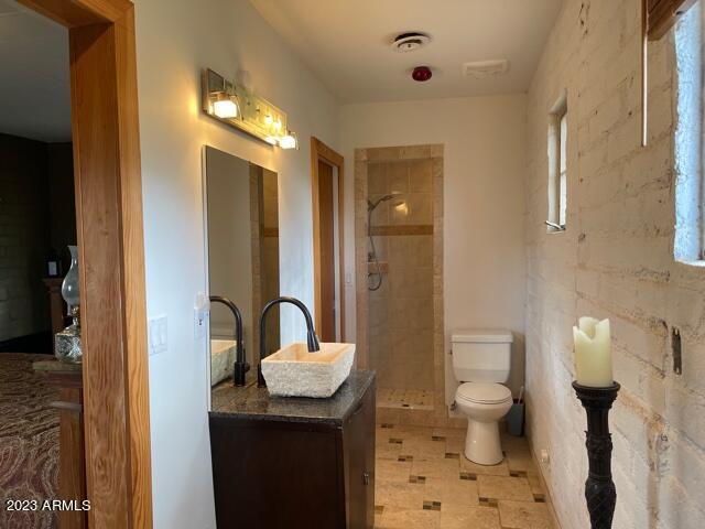 bathroom featuring toilet, vanity with extensive cabinet space, tile flooring, and a tile shower