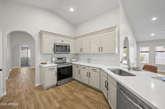 kitchen with light wood-style floors, appliances with stainless steel finishes, arched walkways, and a sink