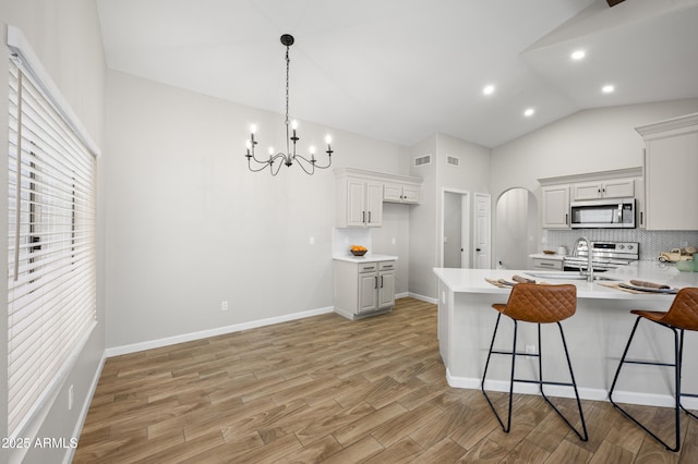 kitchen with arched walkways, stainless steel appliances, vaulted ceiling, light wood-type flooring, and a peninsula