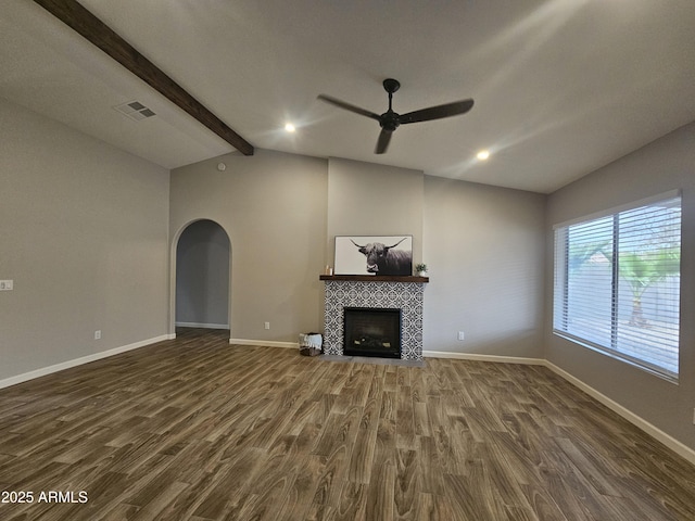 unfurnished living room featuring visible vents, arched walkways, a tile fireplace, lofted ceiling with beams, and dark wood-style floors