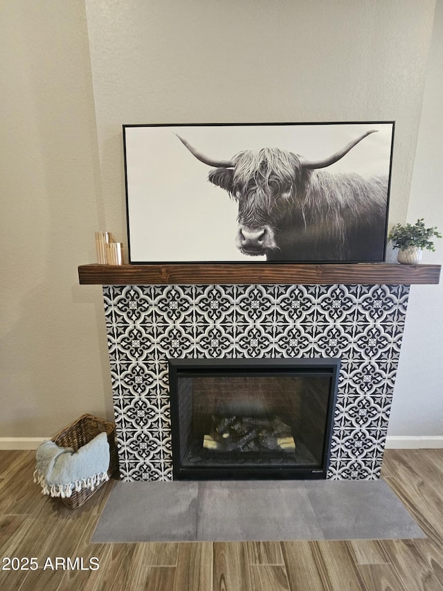 room details featuring a tiled fireplace, baseboards, and wood finished floors