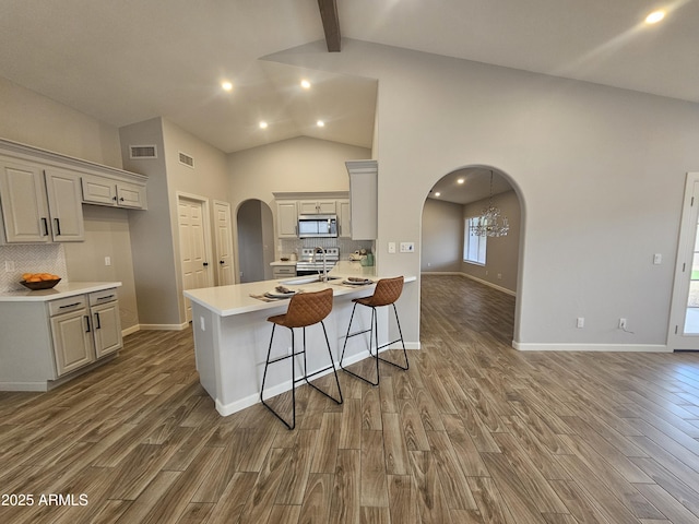 kitchen with arched walkways, light countertops, stainless steel microwave, and wood finished floors