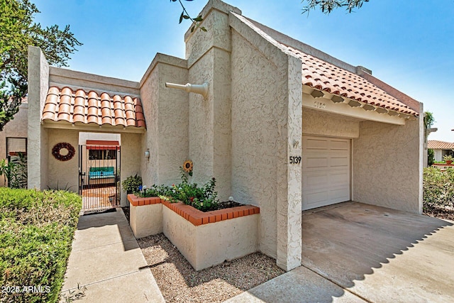 view of front facade featuring an attached garage, a tiled roof, concrete driveway, a gate, and stucco siding