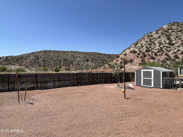 view of yard featuring a shed, a fenced backyard, an outdoor structure, and a mountain view