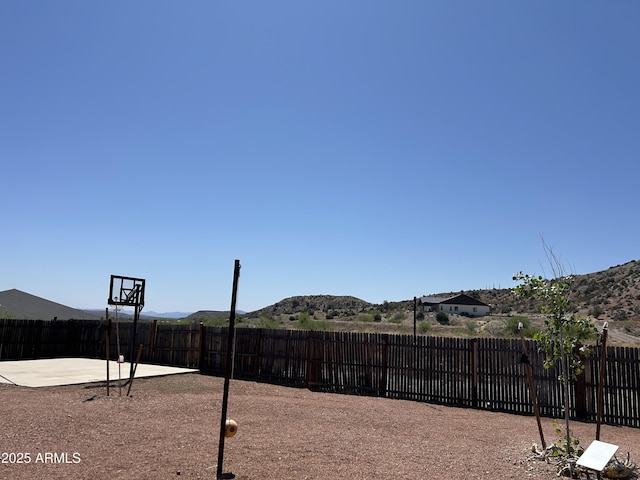 view of yard featuring a mountain view, a fenced backyard, and basketball hoop