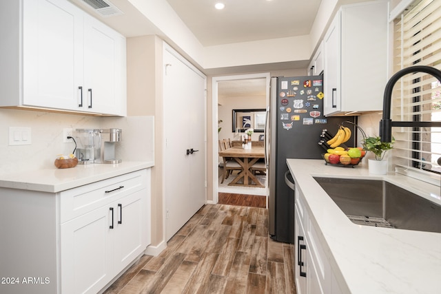 kitchen with backsplash, sink, hardwood / wood-style floors, white cabinetry, and light stone counters