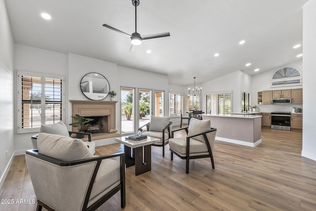 living room featuring ceiling fan with notable chandelier, vaulted ceiling, light hardwood / wood-style floors, and a healthy amount of sunlight