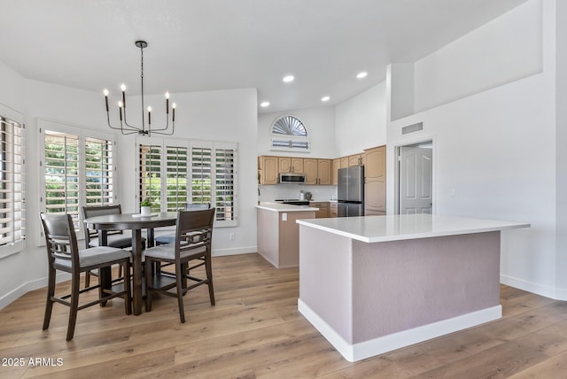 kitchen with light hardwood / wood-style flooring, appliances with stainless steel finishes, high vaulted ceiling, a center island, and decorative light fixtures