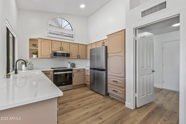 kitchen featuring sink, light wood-type flooring, light brown cabinets, a towering ceiling, and stainless steel appliances