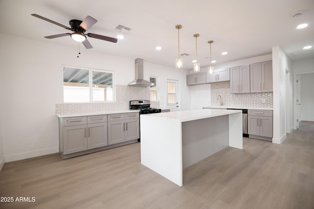 kitchen with wall chimney range hood, light hardwood / wood-style flooring, appliances with stainless steel finishes, a center island, and decorative light fixtures