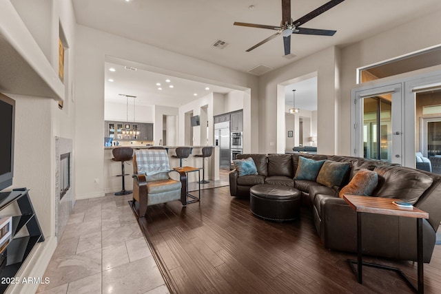 living room featuring ceiling fan with notable chandelier, wood-type flooring, and french doors