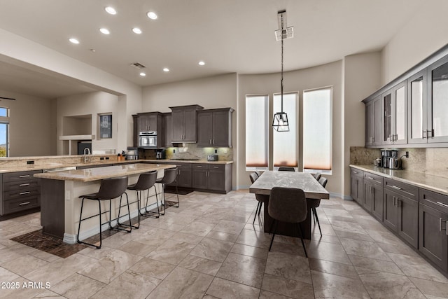 kitchen with light stone countertops, tasteful backsplash, a large island, a kitchen breakfast bar, and decorative light fixtures