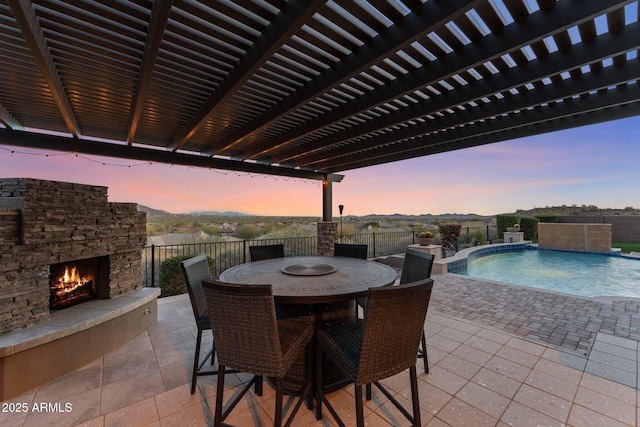 patio terrace at dusk with a fenced in pool, an outdoor stone fireplace, and pool water feature