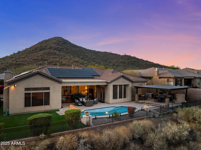 back house at dusk with a mountain view, a patio area, an outdoor hangout area, and solar panels