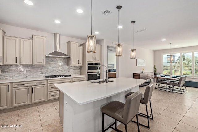 kitchen featuring visible vents, wall chimney exhaust hood, double oven, black cooktop, and a sink