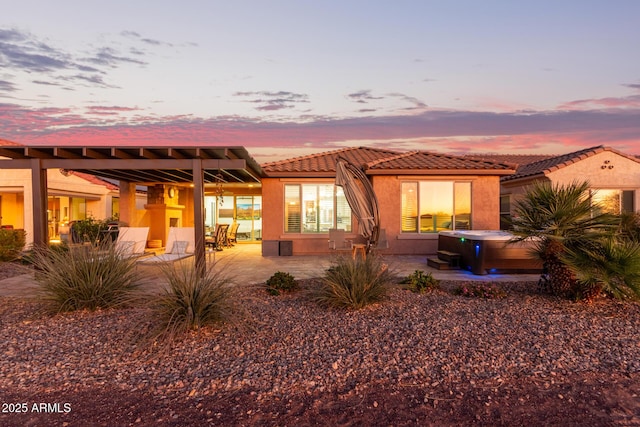 back of house featuring a tiled roof, a patio area, a hot tub, and stucco siding