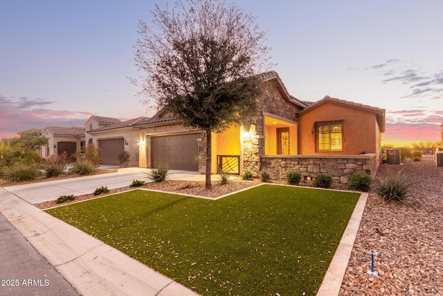 view of front of house with stone siding, a yard, concrete driveway, a tiled roof, and stucco siding