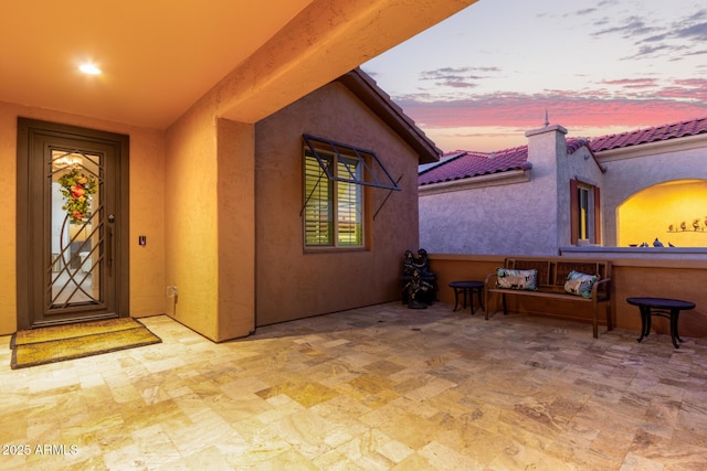 exterior entry at dusk with stucco siding, a patio, and a tiled roof