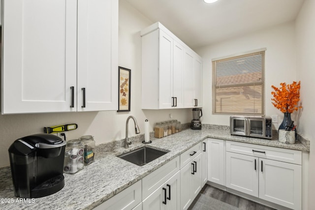 kitchen with sink, dark wood-type flooring, white cabinetry, and light stone countertops