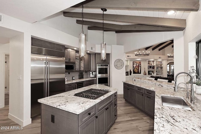 kitchen with a center island, sink, appliances with stainless steel finishes, decorative light fixtures, and light stone counters