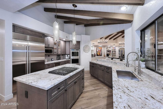 kitchen featuring sink, hanging light fixtures, stainless steel appliances, light stone counters, and dark brown cabinets