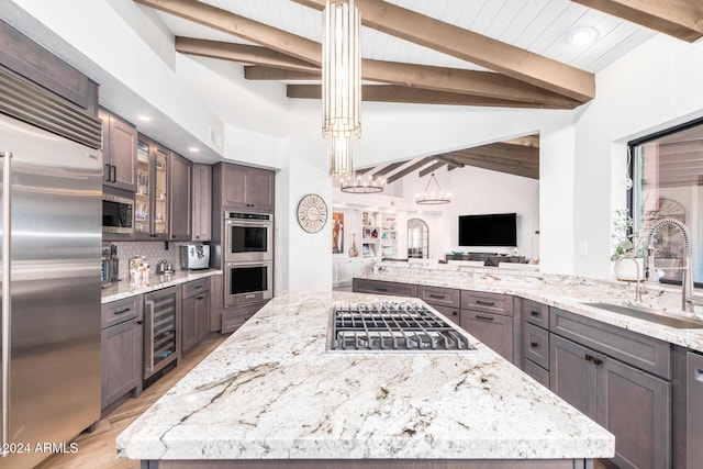 kitchen with light stone countertops, appliances with stainless steel finishes, beverage cooler, sink, and lofted ceiling with beams