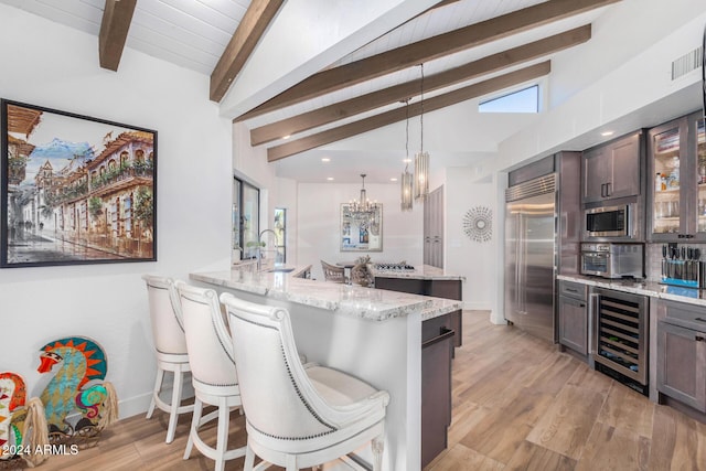 kitchen featuring kitchen peninsula, a breakfast bar, beverage cooler, built in appliances, and light hardwood / wood-style floors