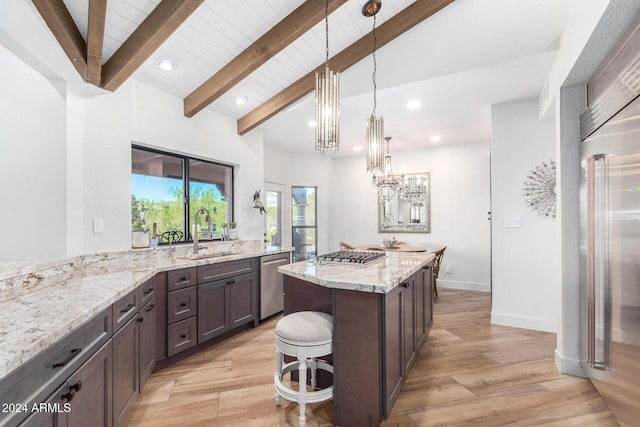 kitchen featuring sink, vaulted ceiling with beams, light stone counters, appliances with stainless steel finishes, and light wood-type flooring