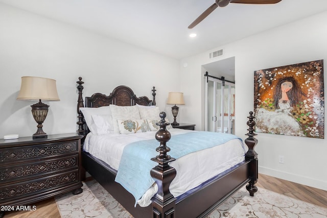 bedroom with a barn door, light hardwood / wood-style floors, and ceiling fan