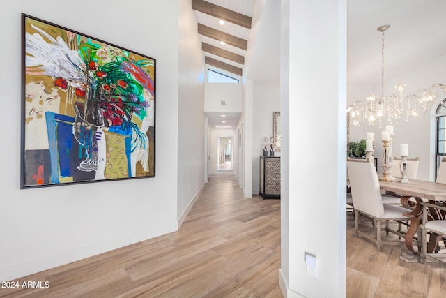 hall with beamed ceiling, light hardwood / wood-style floors, high vaulted ceiling, and a chandelier