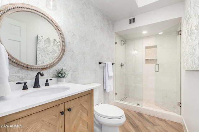 bathroom with toilet, vanity, a shower with shower door, tile walls, and hardwood / wood-style flooring