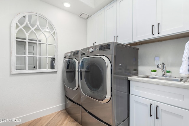 laundry area featuring washing machine and clothes dryer, sink, cabinets, and light hardwood / wood-style floors