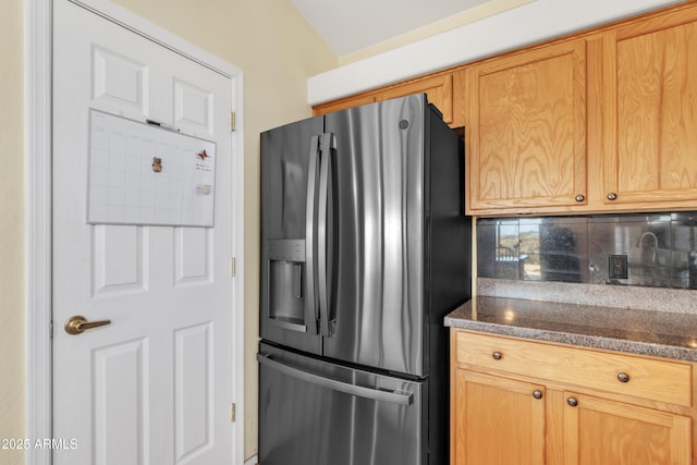 kitchen with stainless steel fridge with ice dispenser, decorative backsplash, and dark stone counters