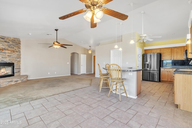 kitchen with a breakfast bar, vaulted ceiling, light carpet, stainless steel appliances, and a fireplace