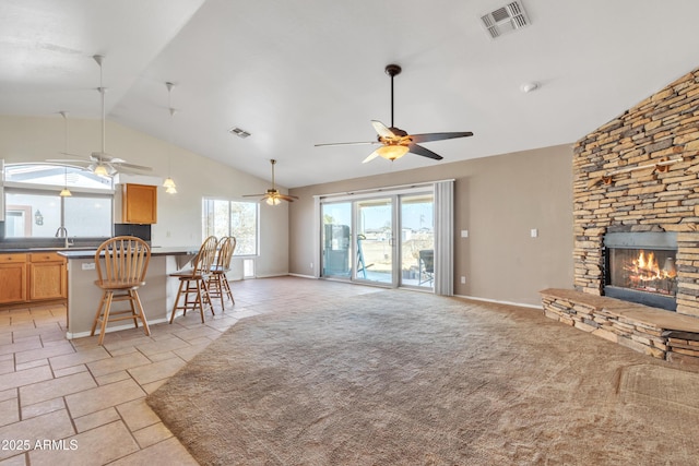 carpeted living room with ceiling fan, a stone fireplace, sink, and high vaulted ceiling