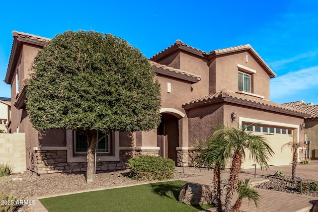 mediterranean / spanish-style house with stucco siding, stone siding, driveway, and a tiled roof