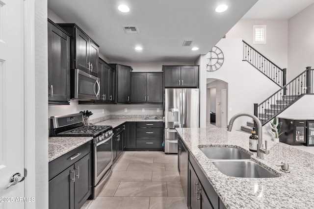 kitchen with a sink, stainless steel appliances, light stone counters, and visible vents