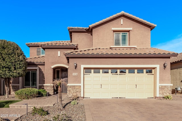 mediterranean / spanish home with stucco siding, stone siding, a tile roof, and decorative driveway