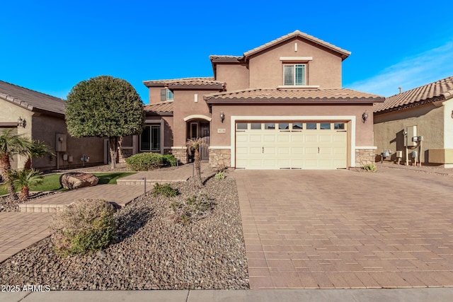 mediterranean / spanish home featuring stucco siding, stone siding, a tile roof, and decorative driveway