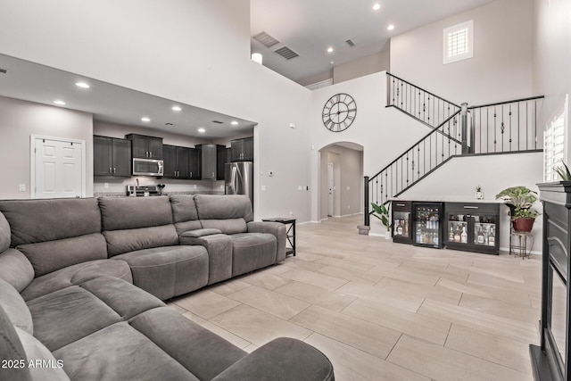 living room featuring visible vents, a high ceiling, recessed lighting, arched walkways, and stairs