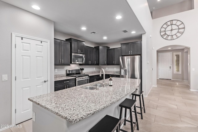 kitchen with a sink, stainless steel appliances, arched walkways, a breakfast bar area, and light stone countertops