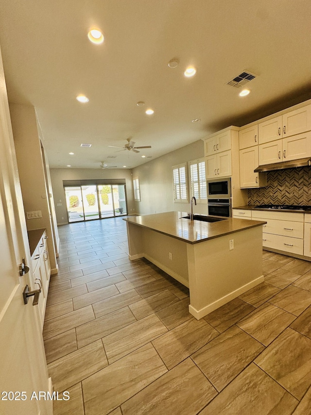 kitchen with appliances with stainless steel finishes, tasteful backsplash, white cabinetry, sink, and a kitchen island with sink