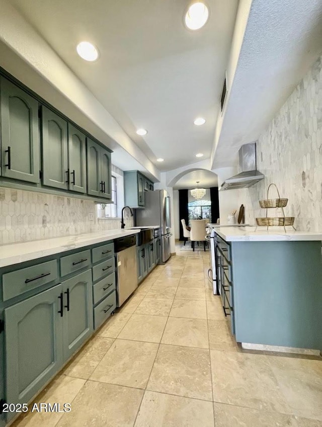 kitchen with appliances with stainless steel finishes, backsplash, wall chimney range hood, light tile patterned floors, and green cabinetry