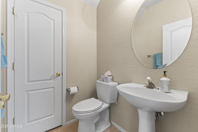 half bathroom with a sink, baseboards, tile patterned flooring, and toilet