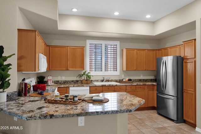 kitchen featuring a peninsula, white appliances, stone countertops, a sink, and light tile patterned floors